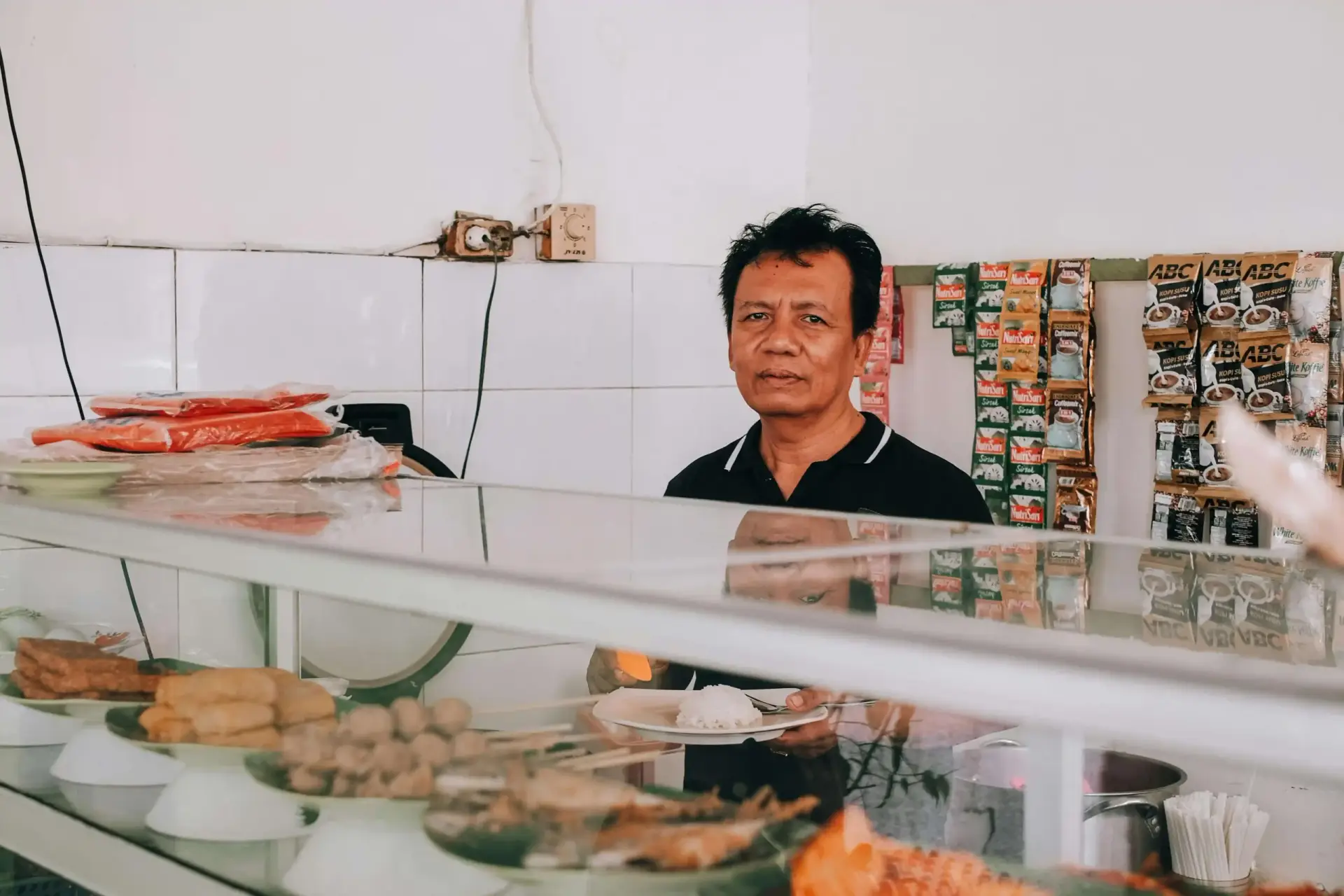 Penjual warung makan berdiri di balik etalase menunggu pelanggan datang sepi pembeli